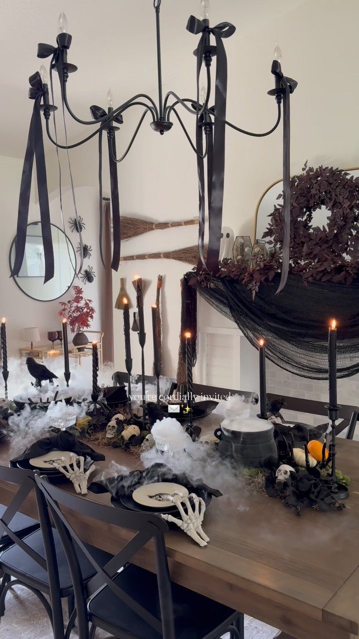 Halloween table setting with skeletal hands, black candles, and fog on wooden table