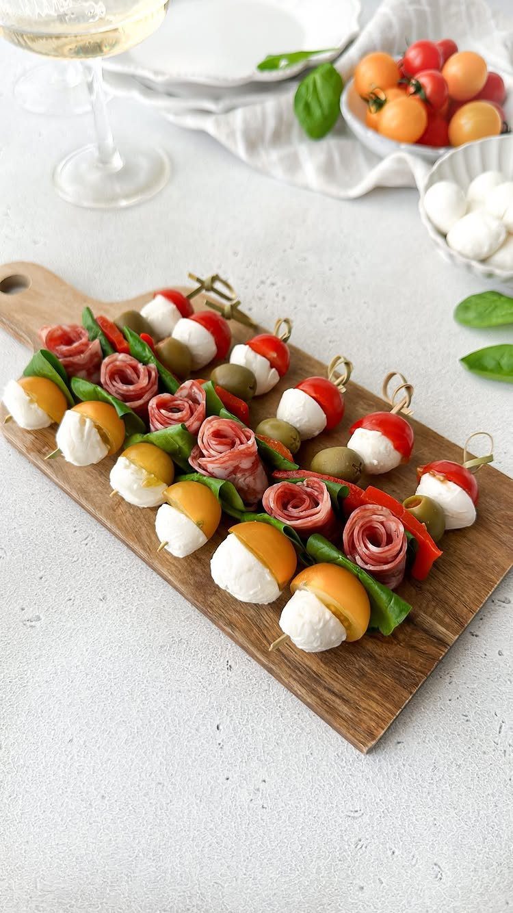 Skewers with mozzarella, cherry tomatoes, rolled salami, and basil on a wooden board.