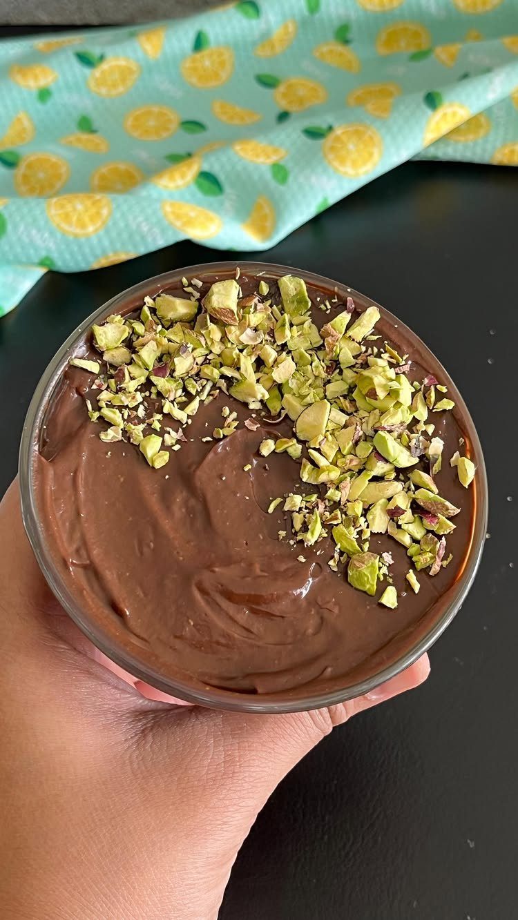Chocolate mousse topped with crushed pistachios in a glass bowl held by a hand.