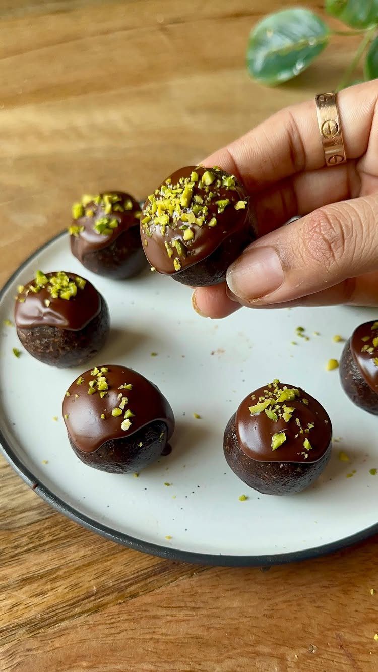 Chocolate bliss balls topped with crushed pistachios on a white ceramic plate.