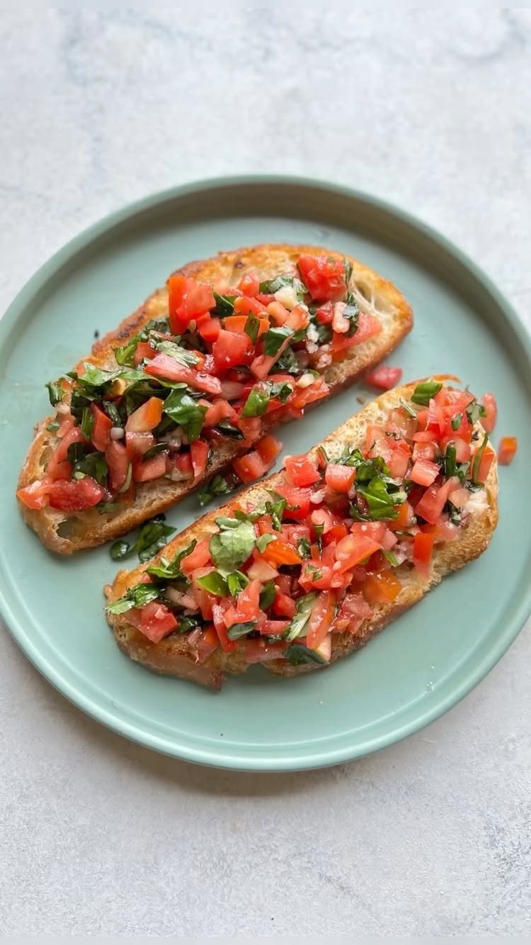 Toasted baguette slices topped with diced tomatoes, basil, and cheese on a plate.