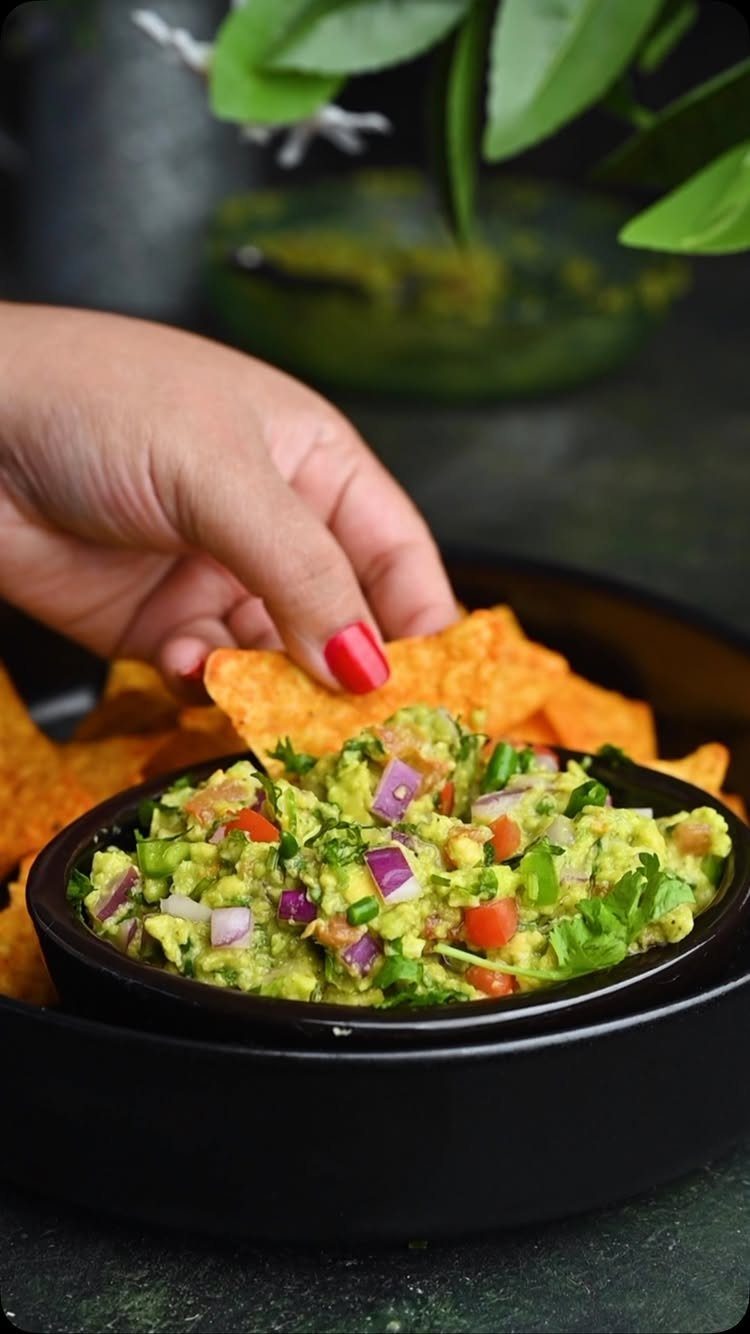 Hand dipping a tortilla chip into a bowl of fresh chunky guacamole
