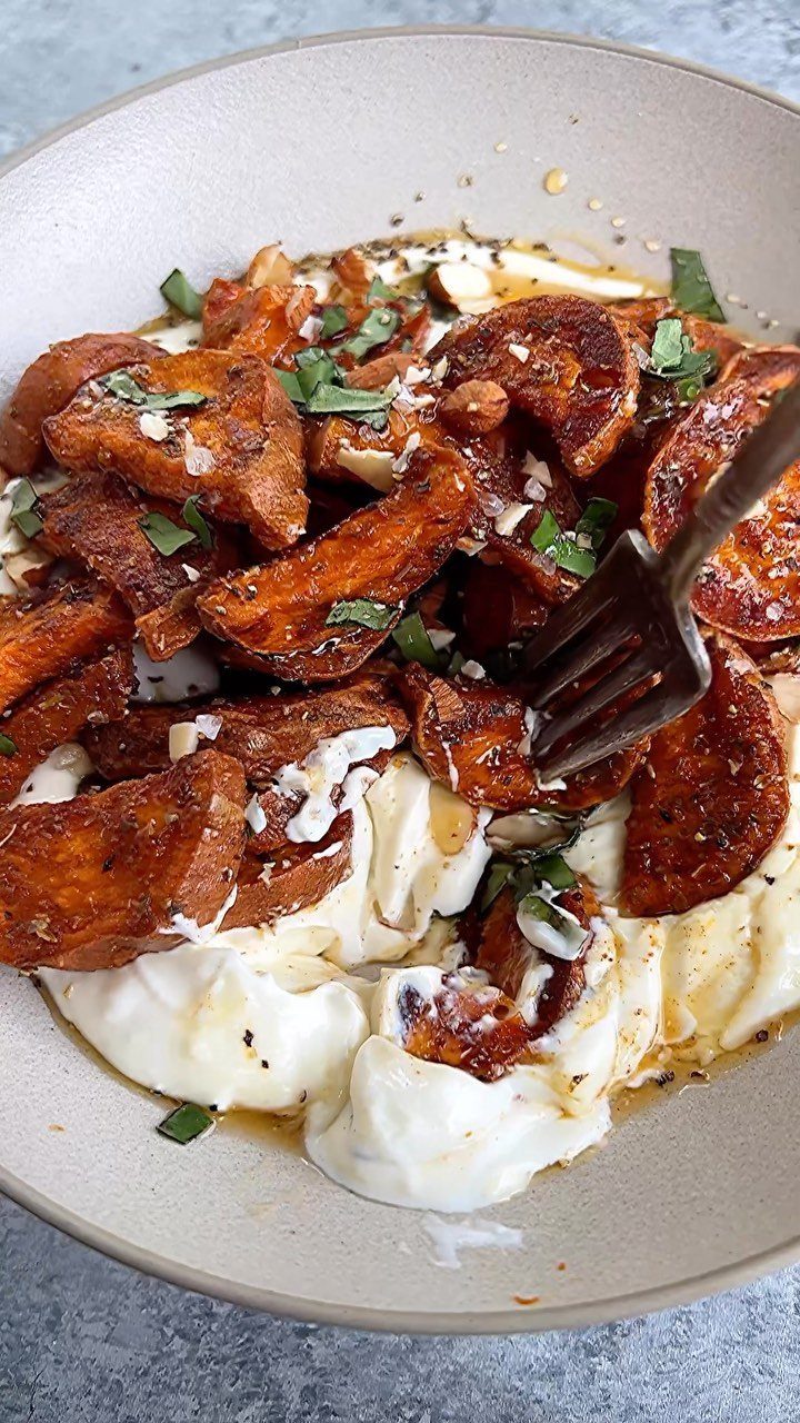 Roasted sweet potato wedges served over creamy white yogurt with fresh green herbs.