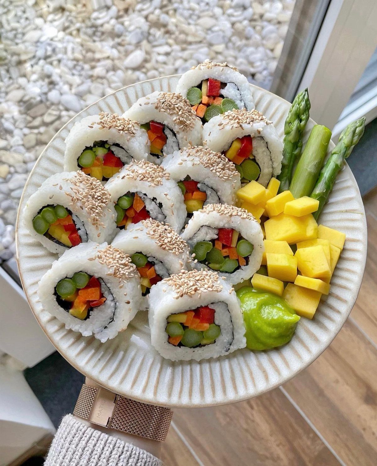 Vegetable sushi rolls with sesame seeds, mango, asparagus, and avocado on a plate.