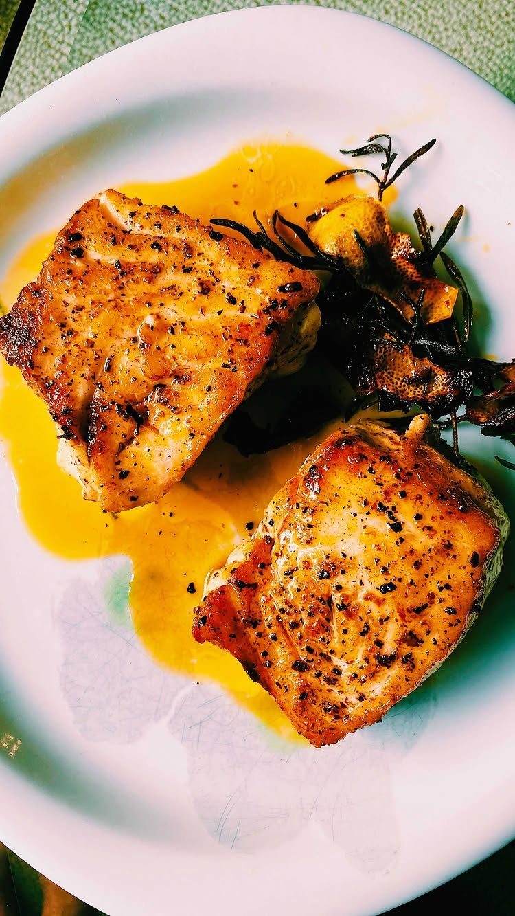 Seared fish fillets in melted butter with roasted garlic and rosemary on white plate