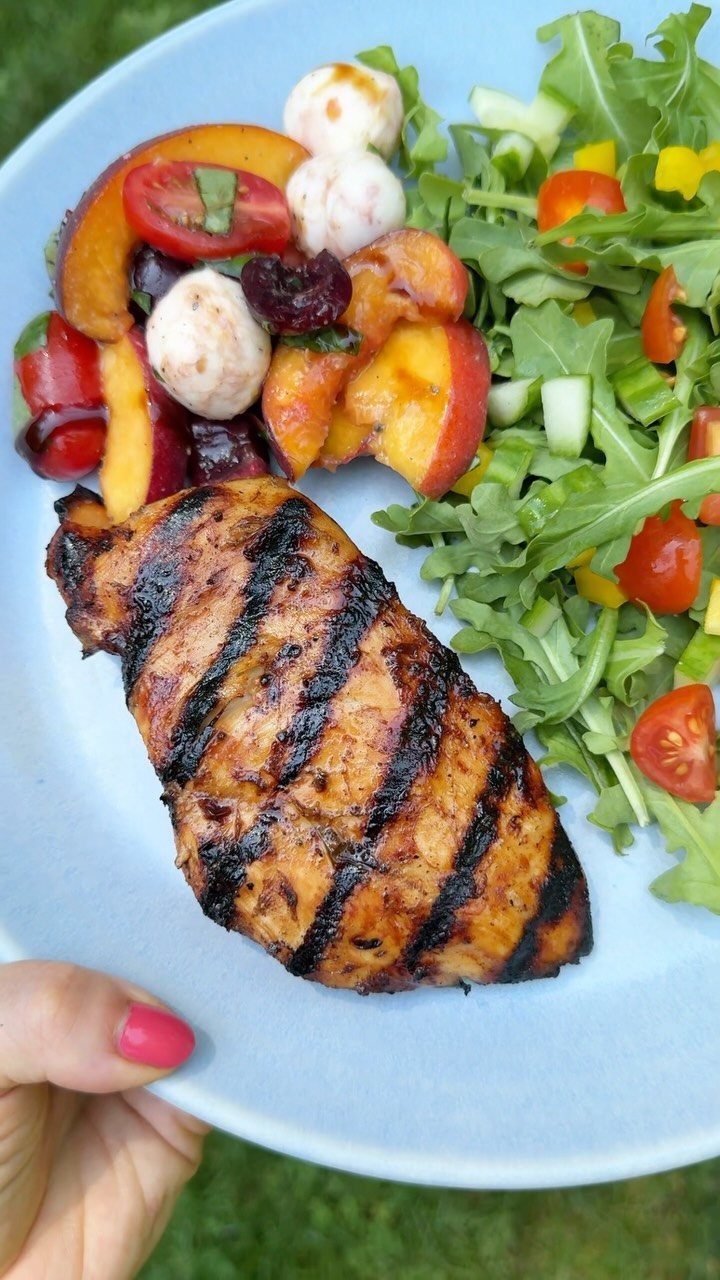 Grilled chicken breast on a blue plate with fresh garden and fruit salads.