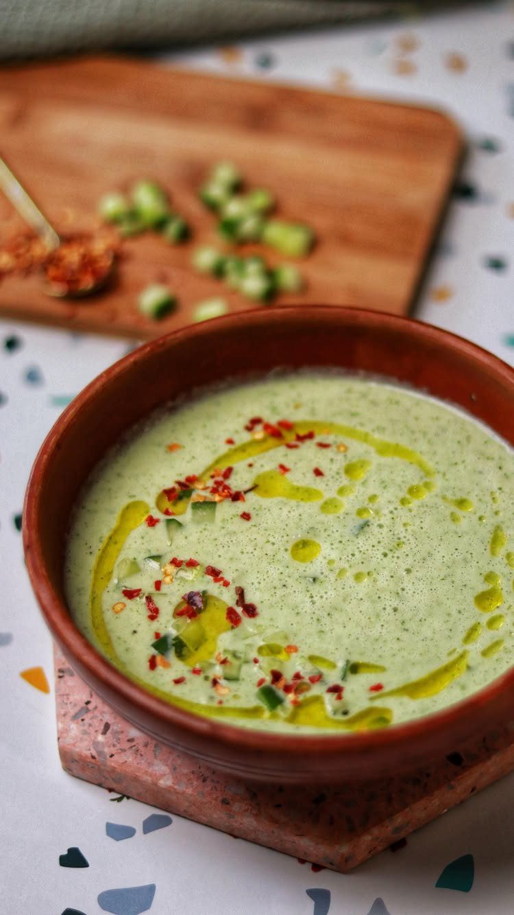 Creamy green cucumber gazpacho soup in a brown bowl topped with olive oil.