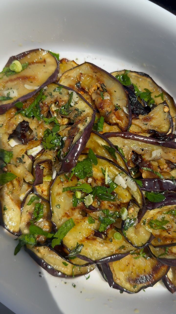 Grilled eggplant slices with fresh green herbs and garlic in a white bowl.