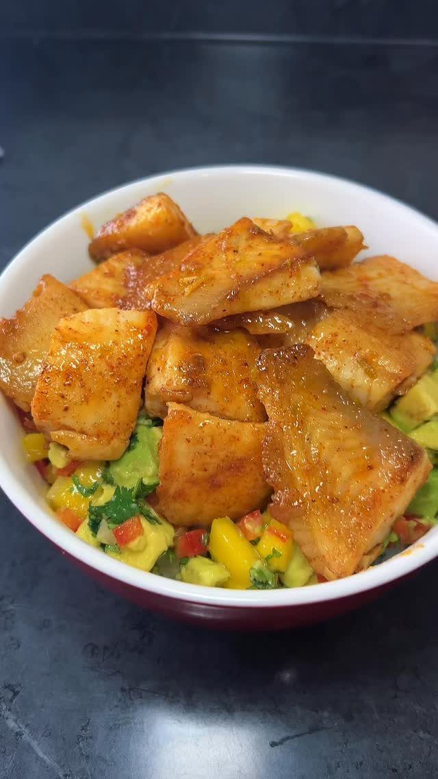 Glazed white fish fillets served over a mango and avocado salsa in a bowl.