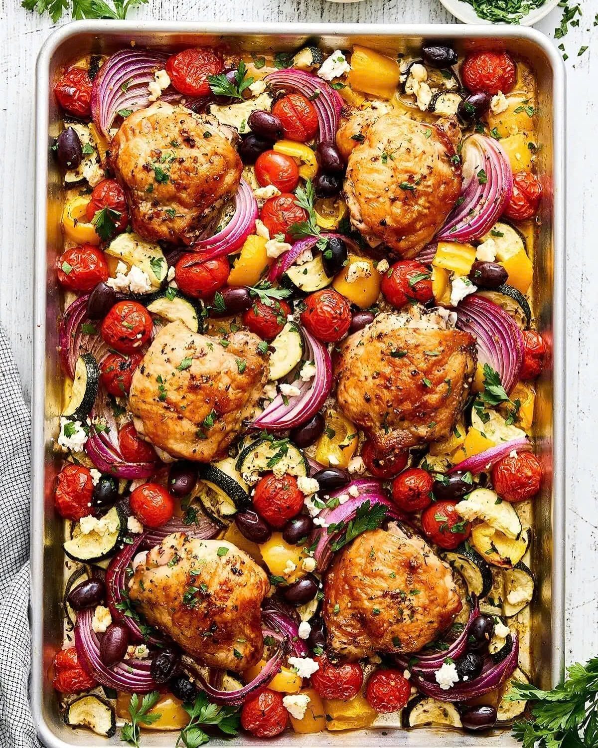 Roasted chicken thighs and colorful vegetables on a silver sheet pan with feta.