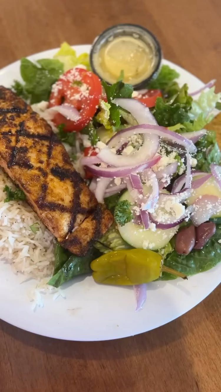 Grilled salmon fillet served with a fresh Greek salad on a white plate.