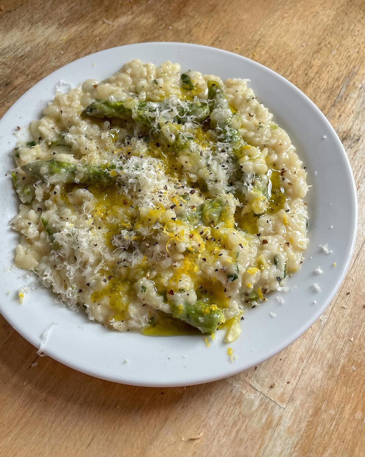 Creamy risotto with asparagus, parmesan cheese, and lemon zest on a white plate.