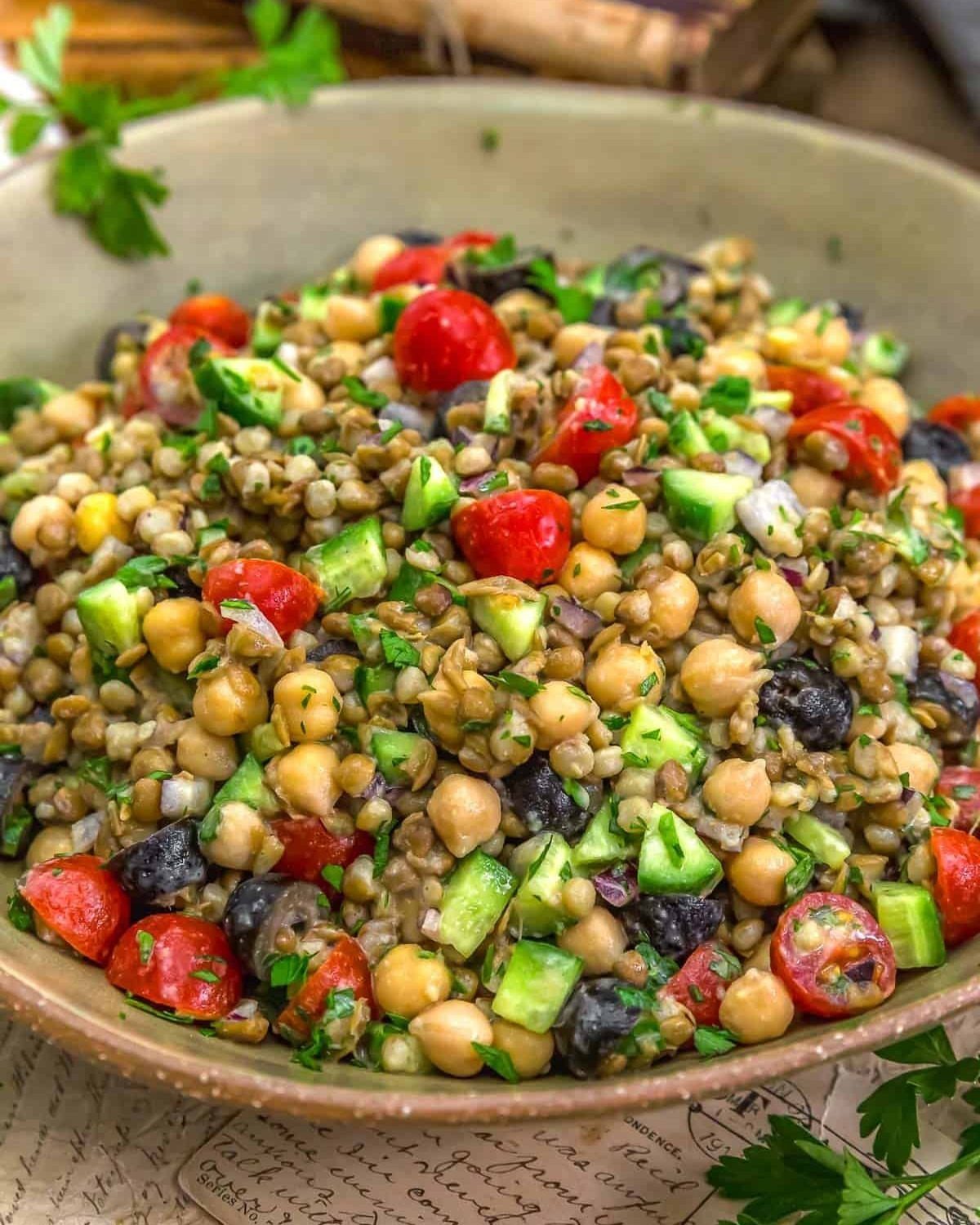 Lentil salad with chickpeas, cherry tomatoes, cucumbers, and olives in a ceramic bowl.