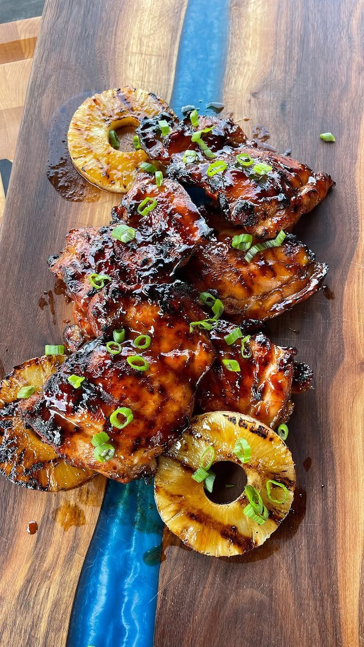 Grilled glazed chicken and charred pineapple rings on a wooden board with green onions