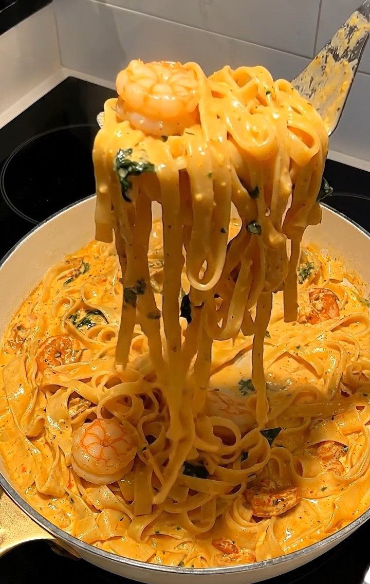 Fettuccine pasta with shrimp and spinach in a creamy orange sauce being lifted.
