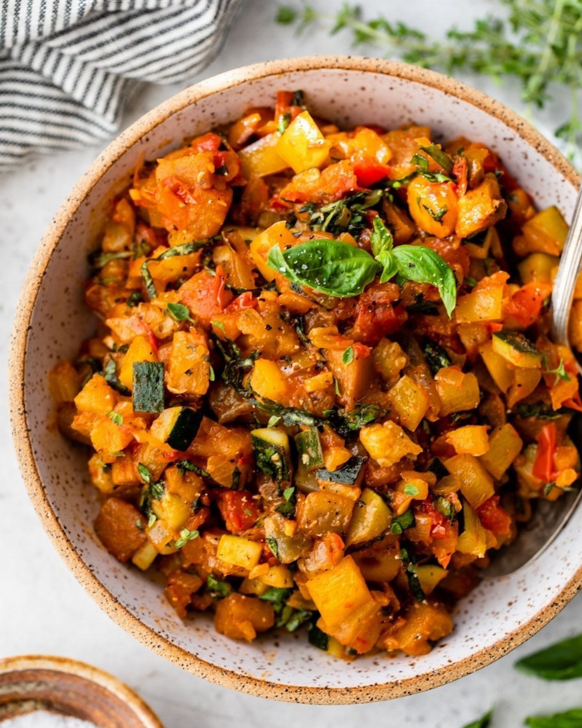 Ratatouille with diced summer vegetables and fresh basil in a ceramic bowl
