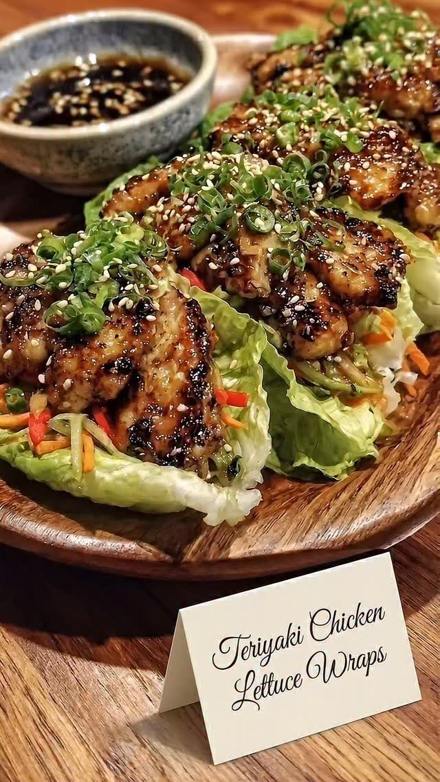 Teriyaki chicken lettuce wraps topped with sesame seeds and green onions on wood.