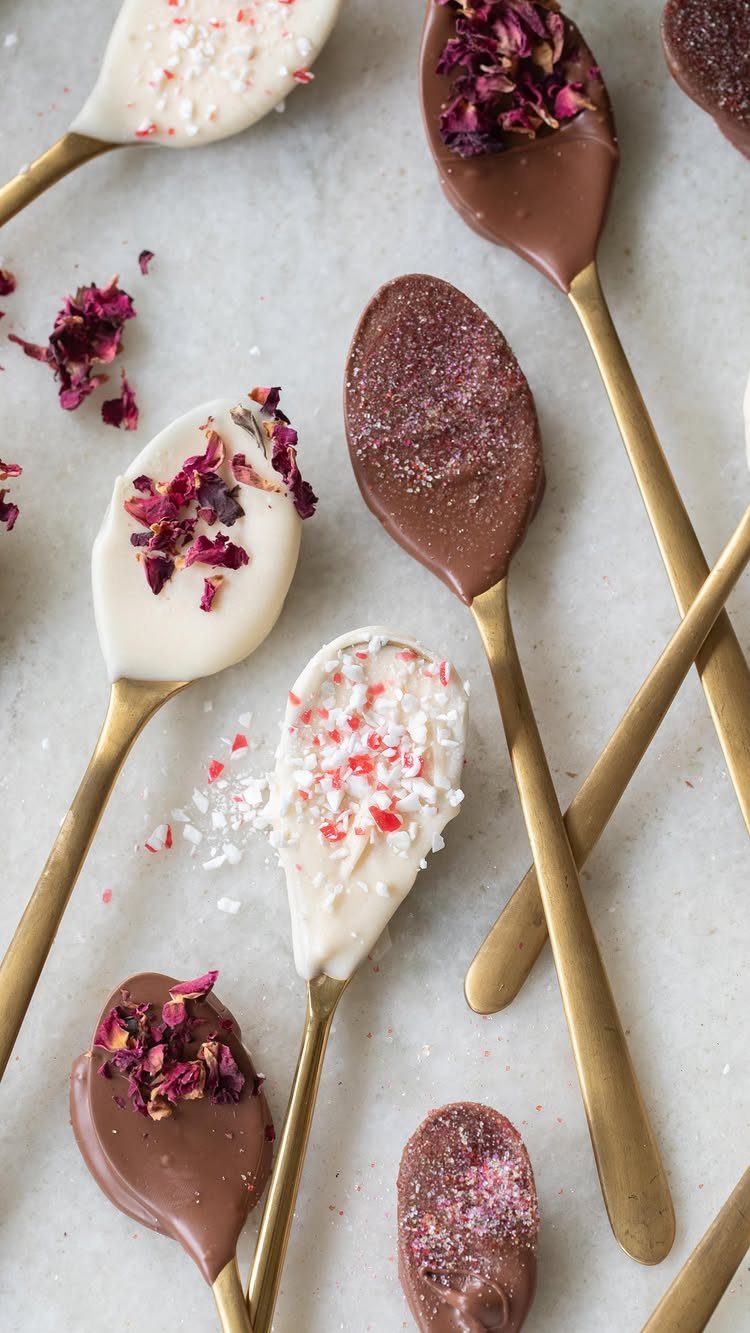 Chocolate dipped spoons with rose petals and peppermint on a marble surface