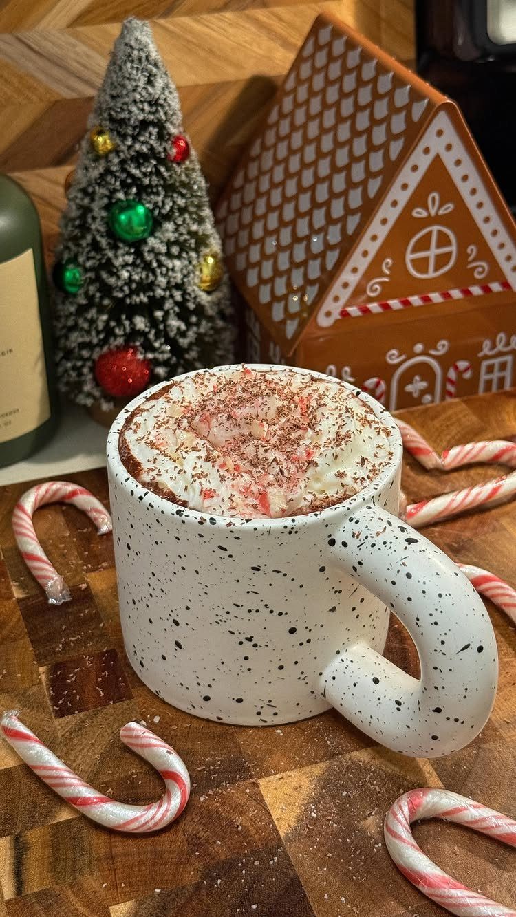 Hot chocolate with whipped cream in a speckled mug surrounded by candy canes.
