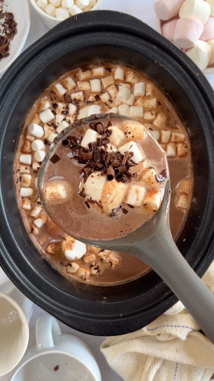 Hot chocolate with marshmallows and chocolate shavings in a black slow cooker.