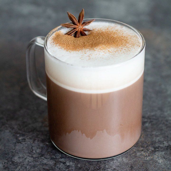 Hot chocolate in a glass mug topped with foam and star anise.