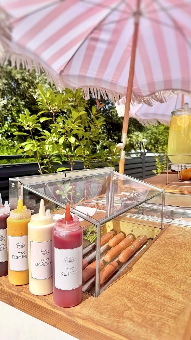 Grilled hot dogs in a clear case with condiment bottles on a wooden table.