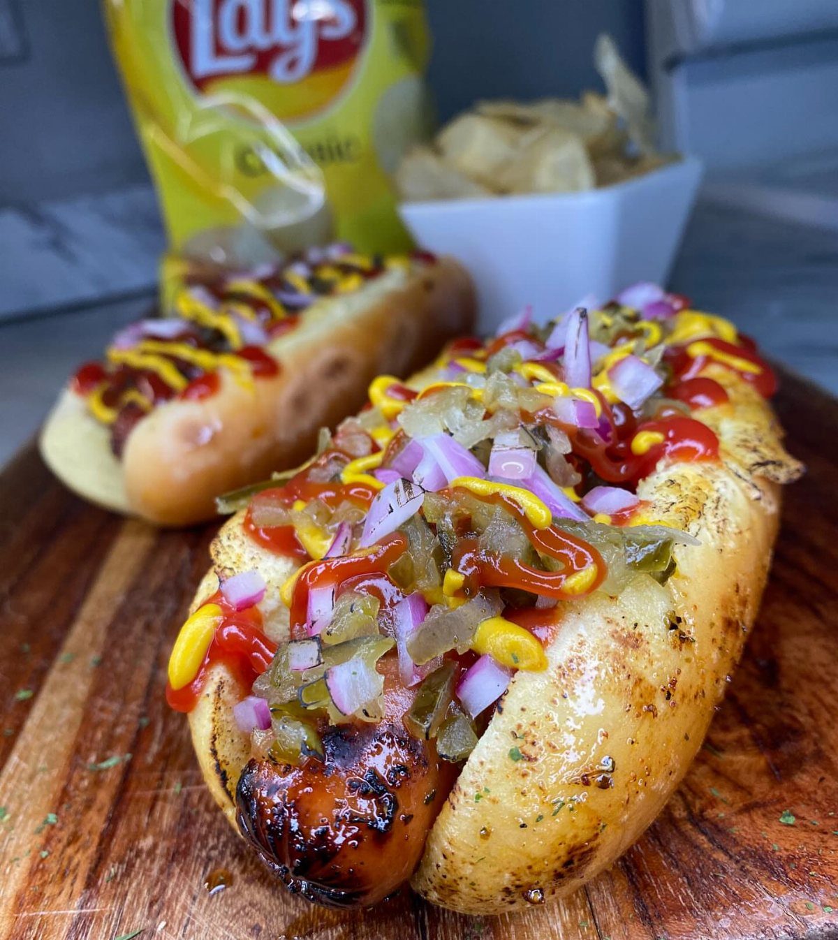 Grilled hot dogs topped with ketchup, mustard, relish, and red onions on wood.