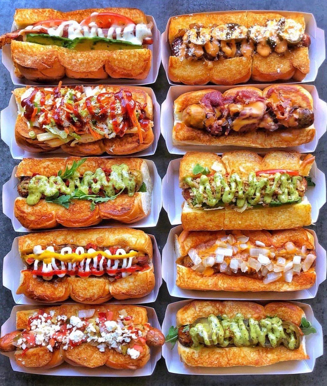 Ten gourmet hot dogs with diverse toppings arranged in white cardboard trays.