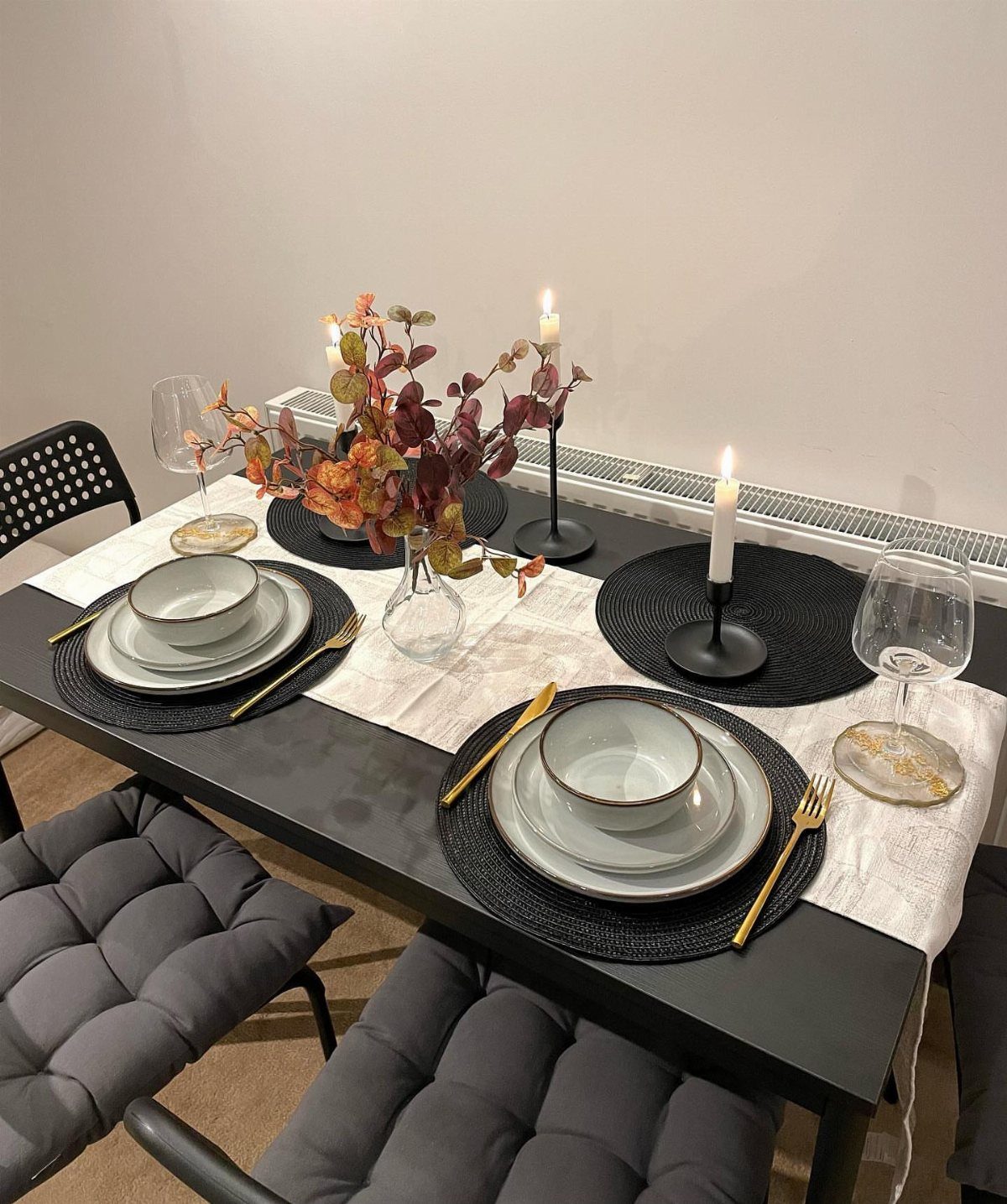 Dining table set with white plates, gold cutlery, and autumn leaf centerpiece.