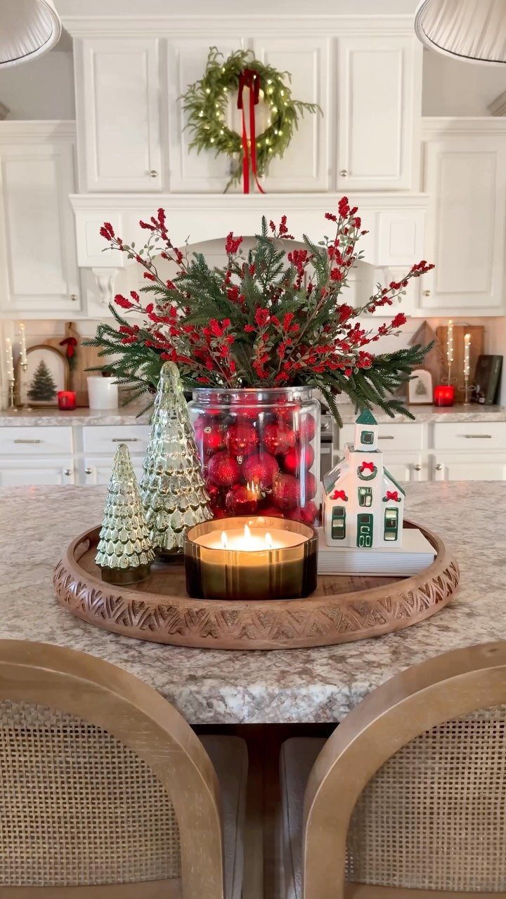 Holiday centerpiece with red ornaments, greenery, and a candle on a wooden tray.