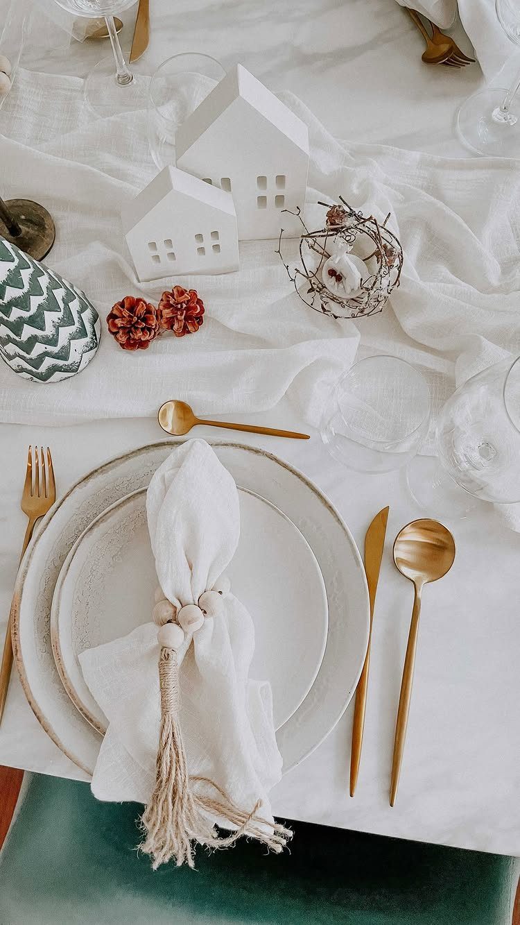 White plates and gold cutlery arranged on a white tablecloth with decorative miniatures.