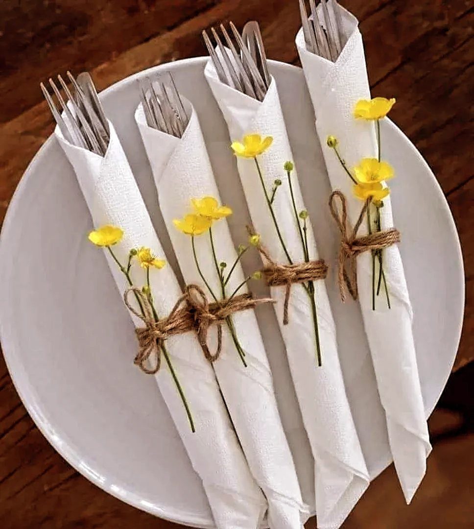 Cutlery wrapped in white napkins with twine and yellow flowers on a plate.