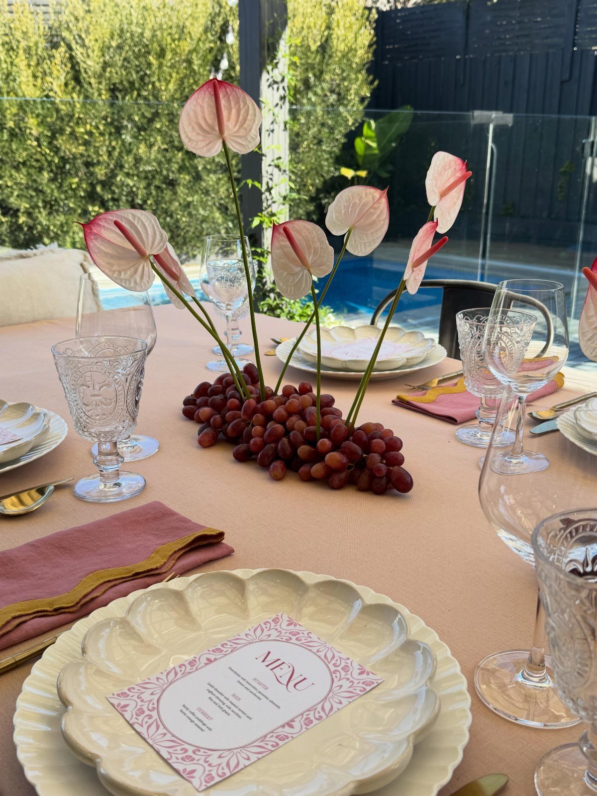 Elegant outdoor table setting with peach linens, white plates, and floral centerpiece.