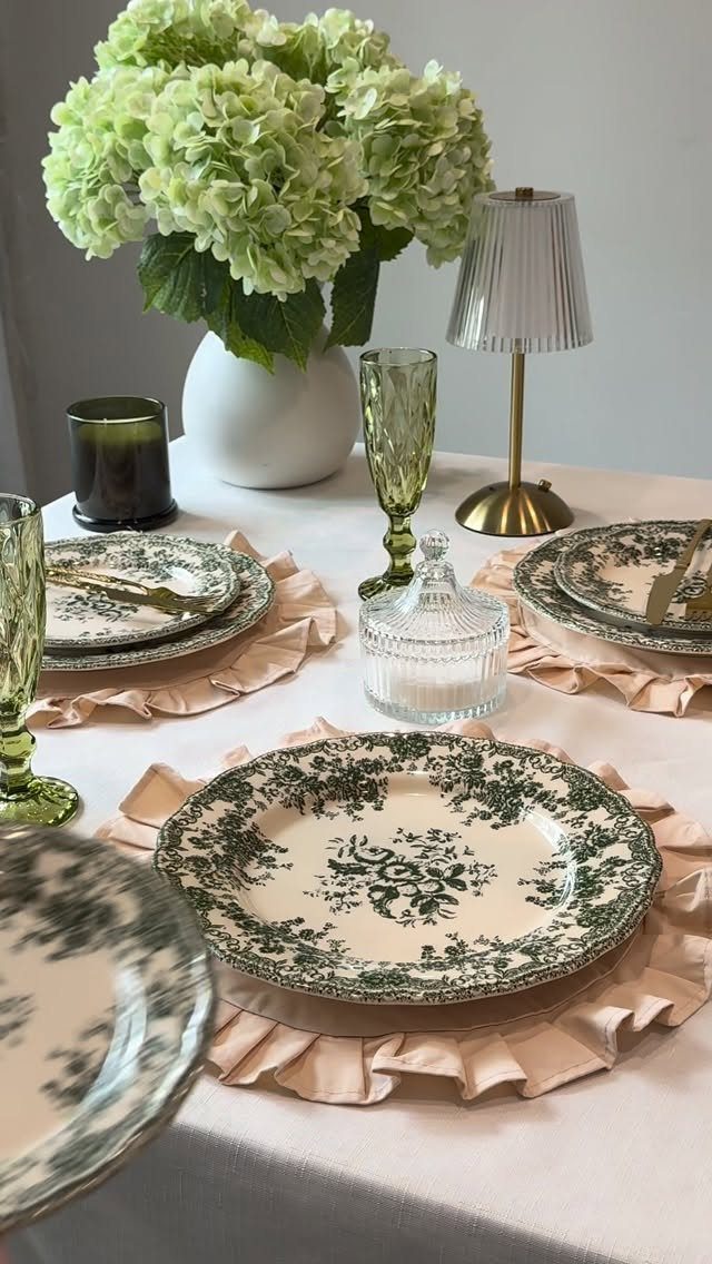 Floral plates and green glasses on ruffled peach placemats with green hydrangeas.