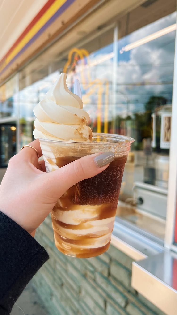 Ice cream float in a plastic cup held against a store window background.