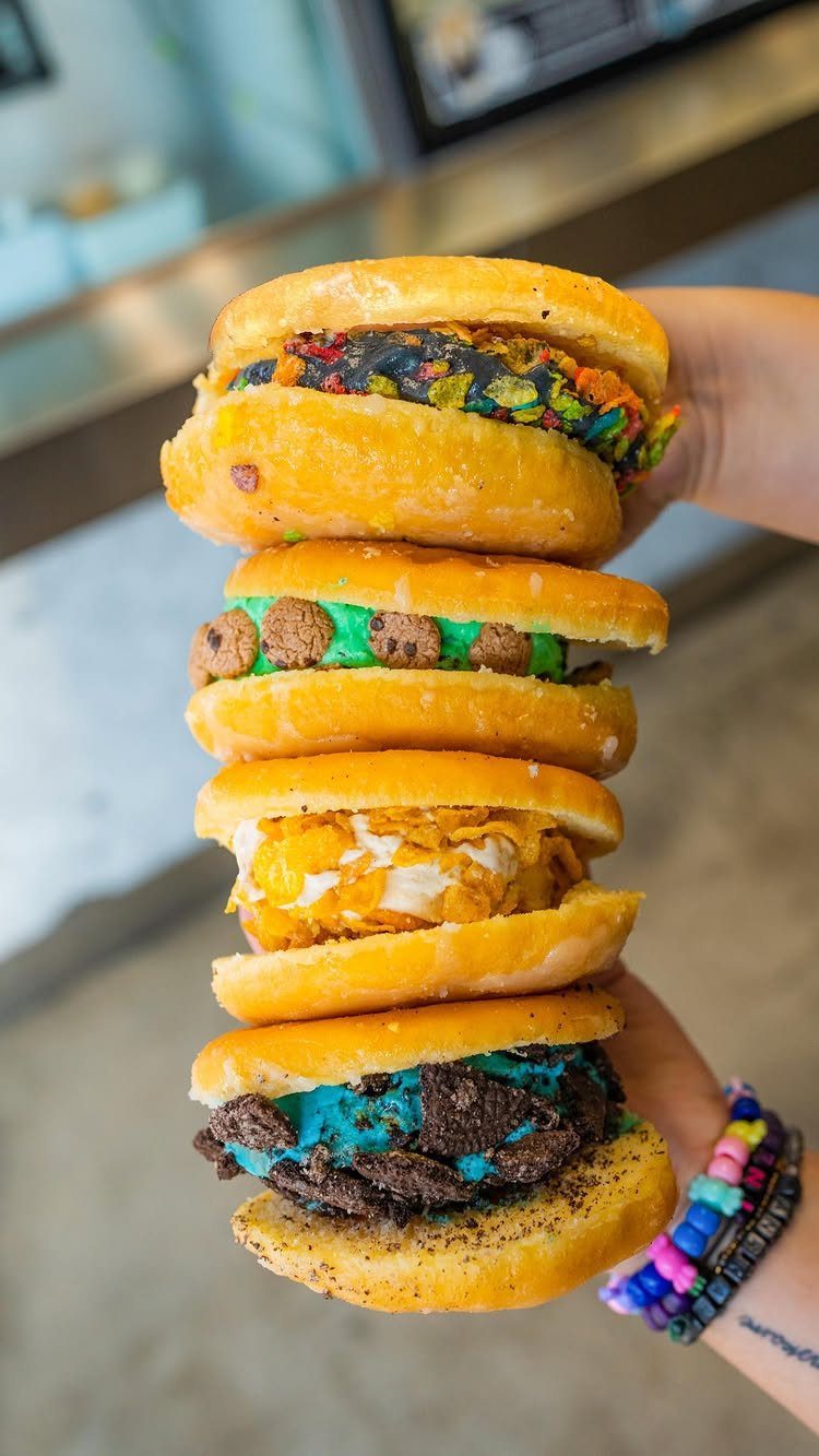 Stacked donut ice cream sandwiches with colorful fillings held by a hand.