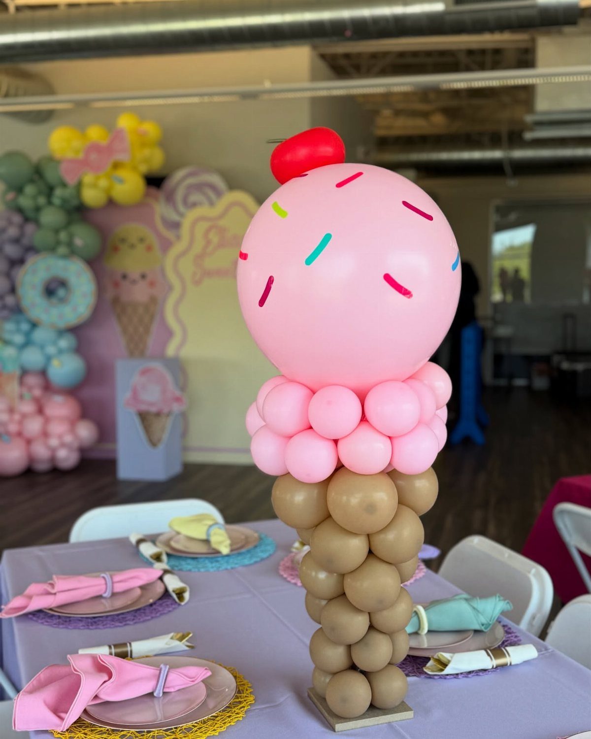 Balloon ice cream cone centerpiece on a purple table with party place settings.