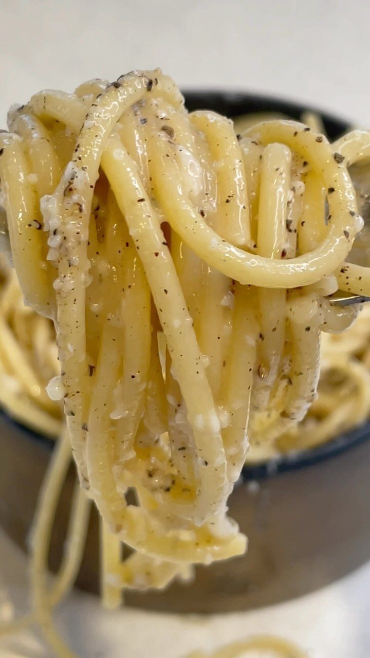 Creamy pasta with black pepper lifted by a fork from a dark bowl.