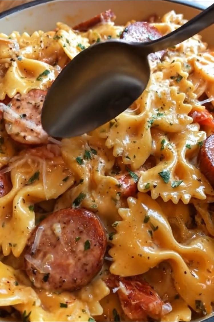 Farfalle pasta with sliced sausage in a creamy sauce with parsley and cheese.