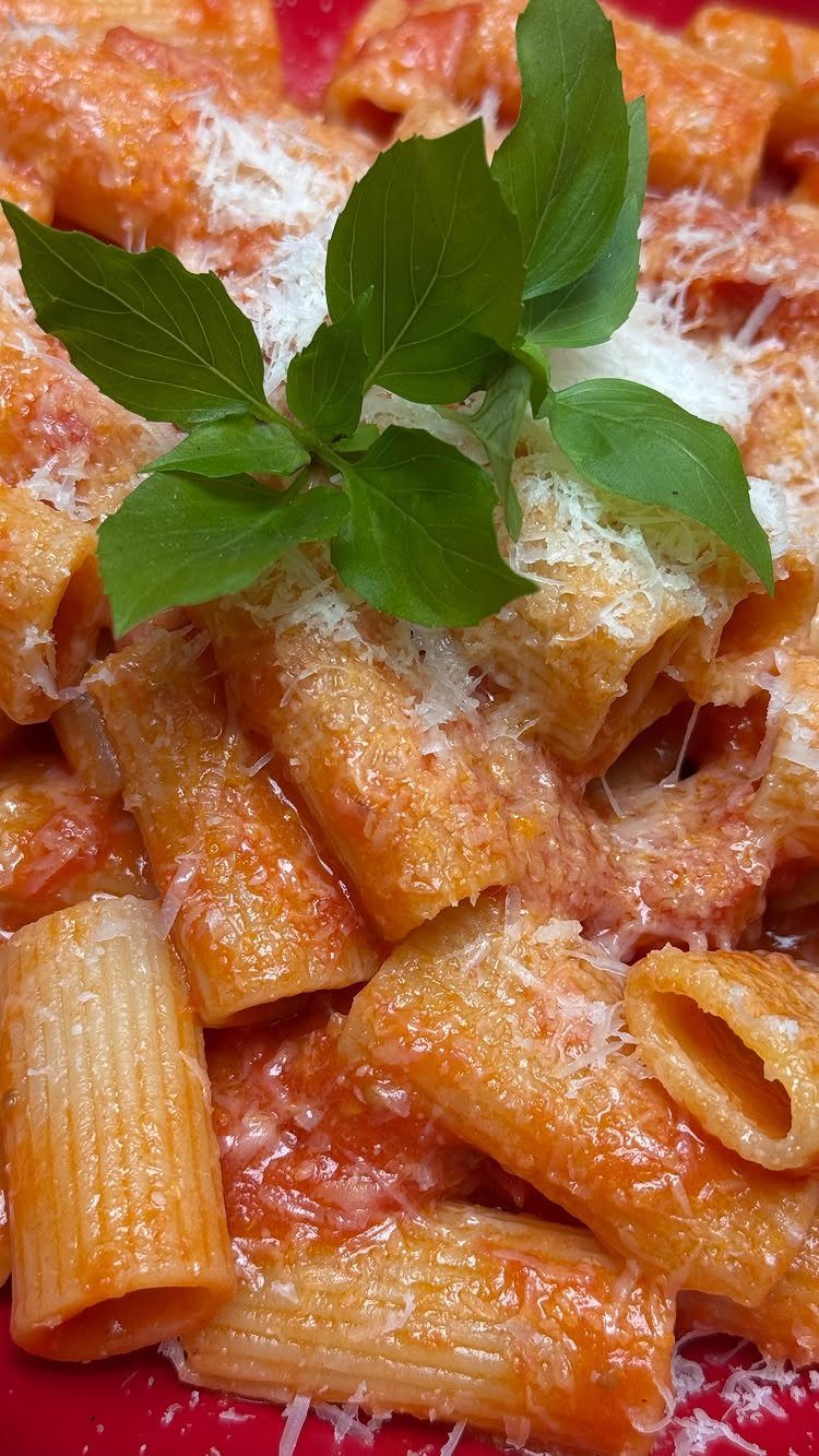 Rigatoni pasta with red tomato sauce, grated cheese, and fresh basil leaves.