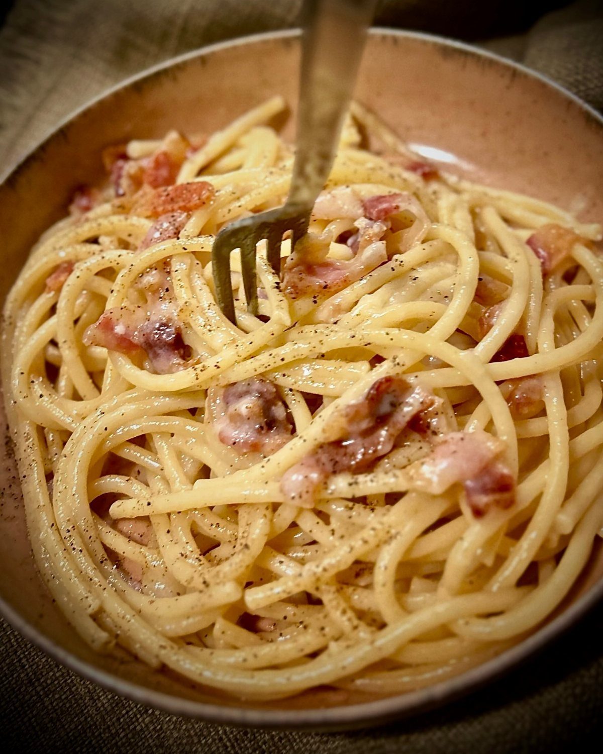Creamy pasta with pancetta and black pepper in a bowl with a fork.