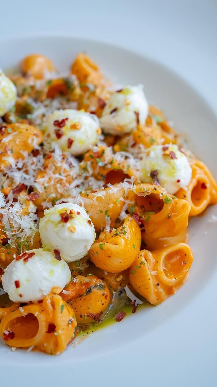 Pasta shells with orange sauce, mozzarella balls, and grated cheese on a white plate.