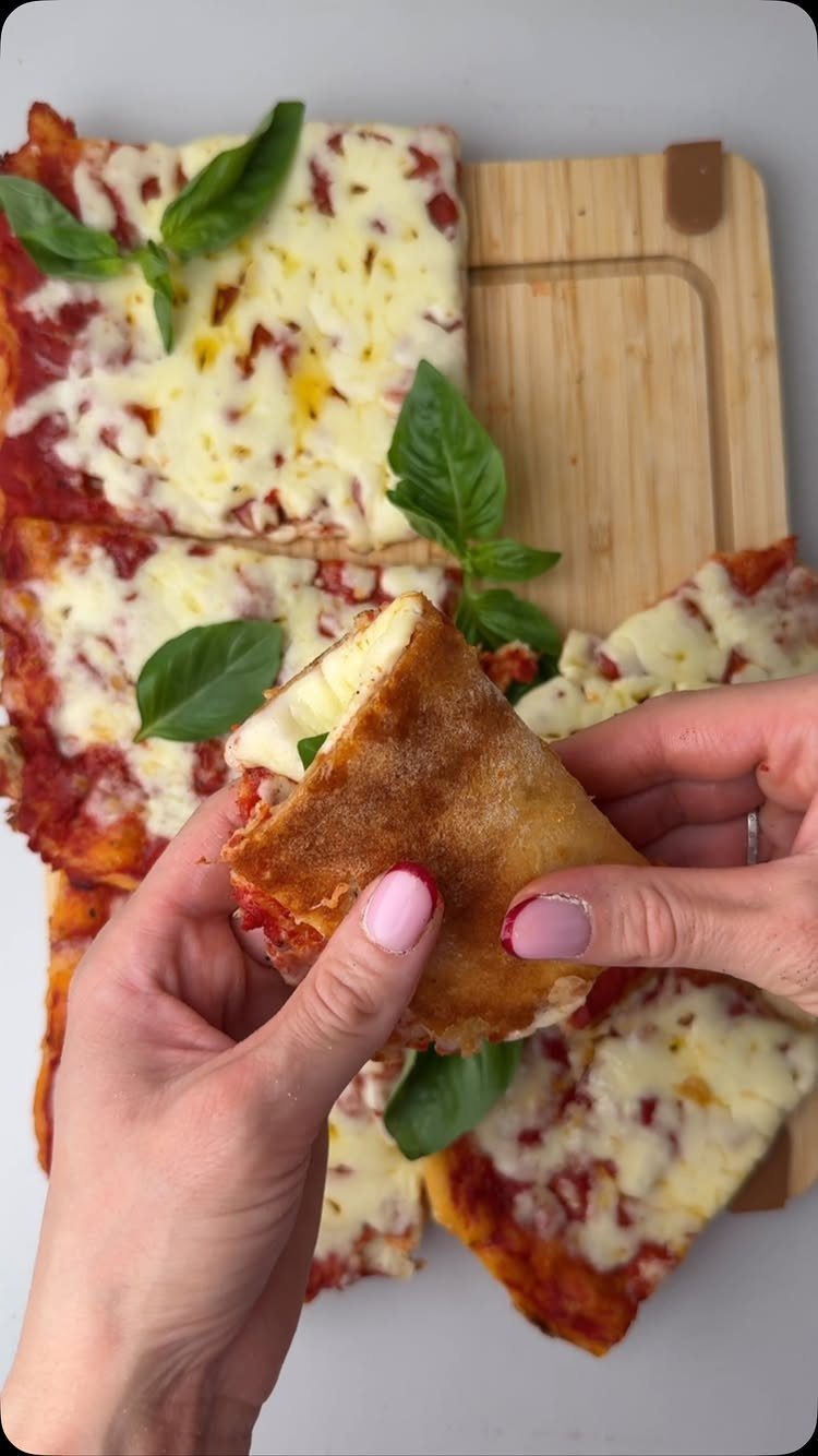 Pizza Margherita slices with melted mozzarella and fresh basil on a wooden board.