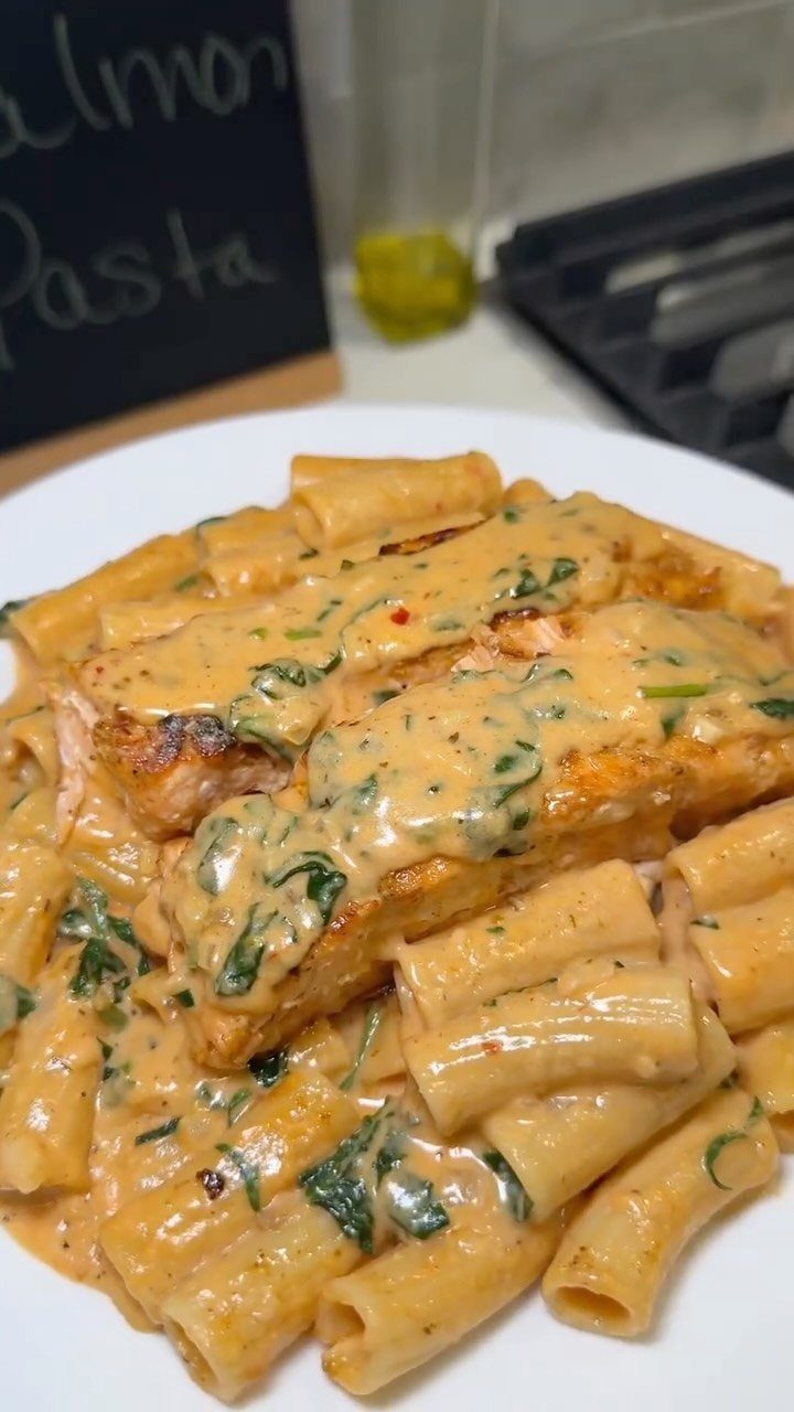 Rigatoni pasta and salmon fillets topped with creamy spinach sauce on white plate