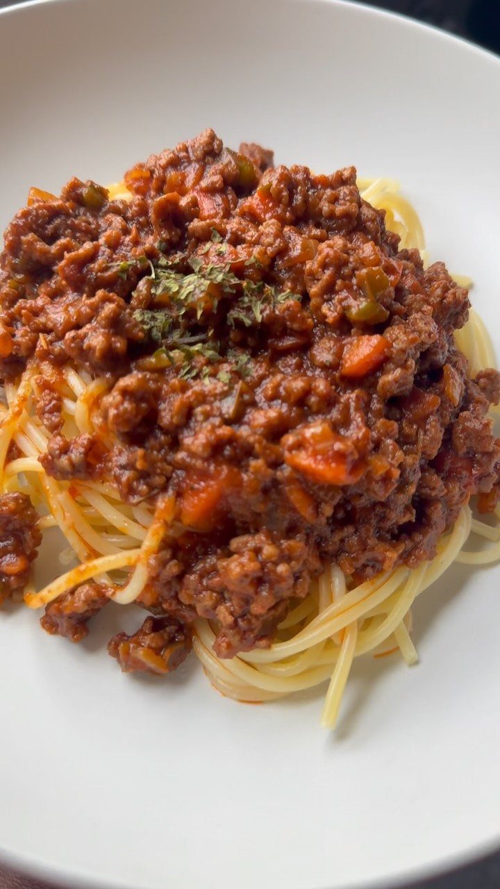 Spaghetti topped with a hearty meat bolognese sauce in a white bowl.