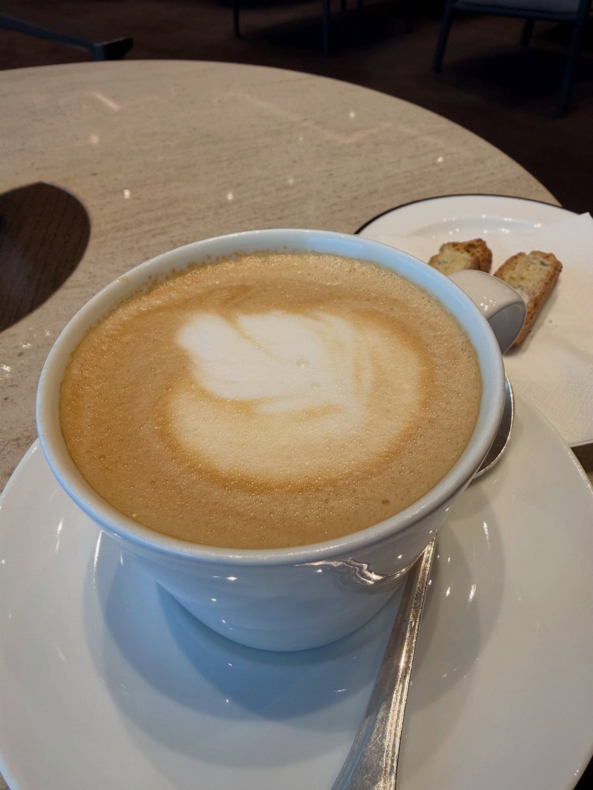 Cappuccino with latte art in a white cup served with biscotti cookies.