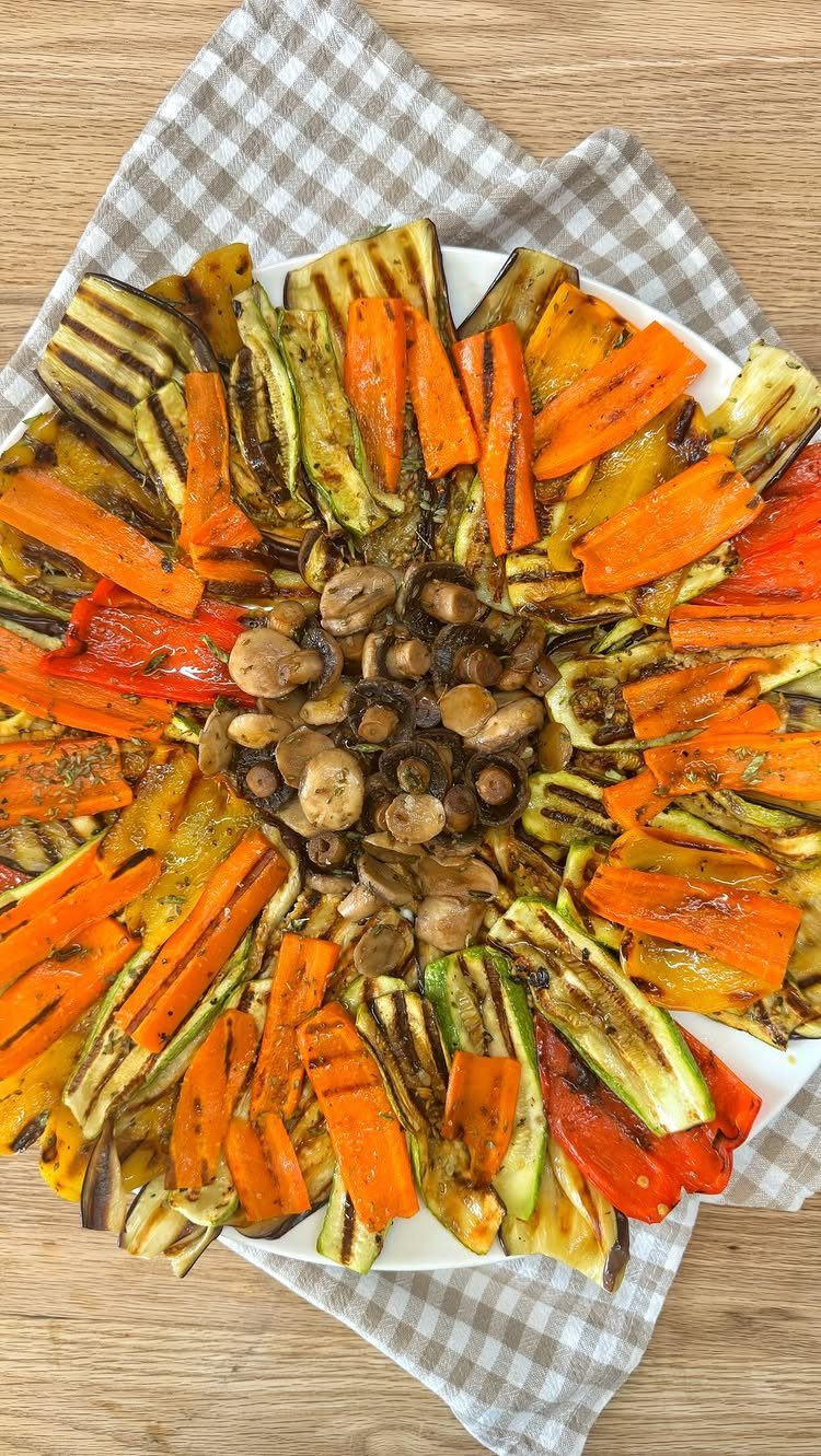 Grilled carrots, zucchini, and red peppers arranged around sautéed mushrooms on a plate.