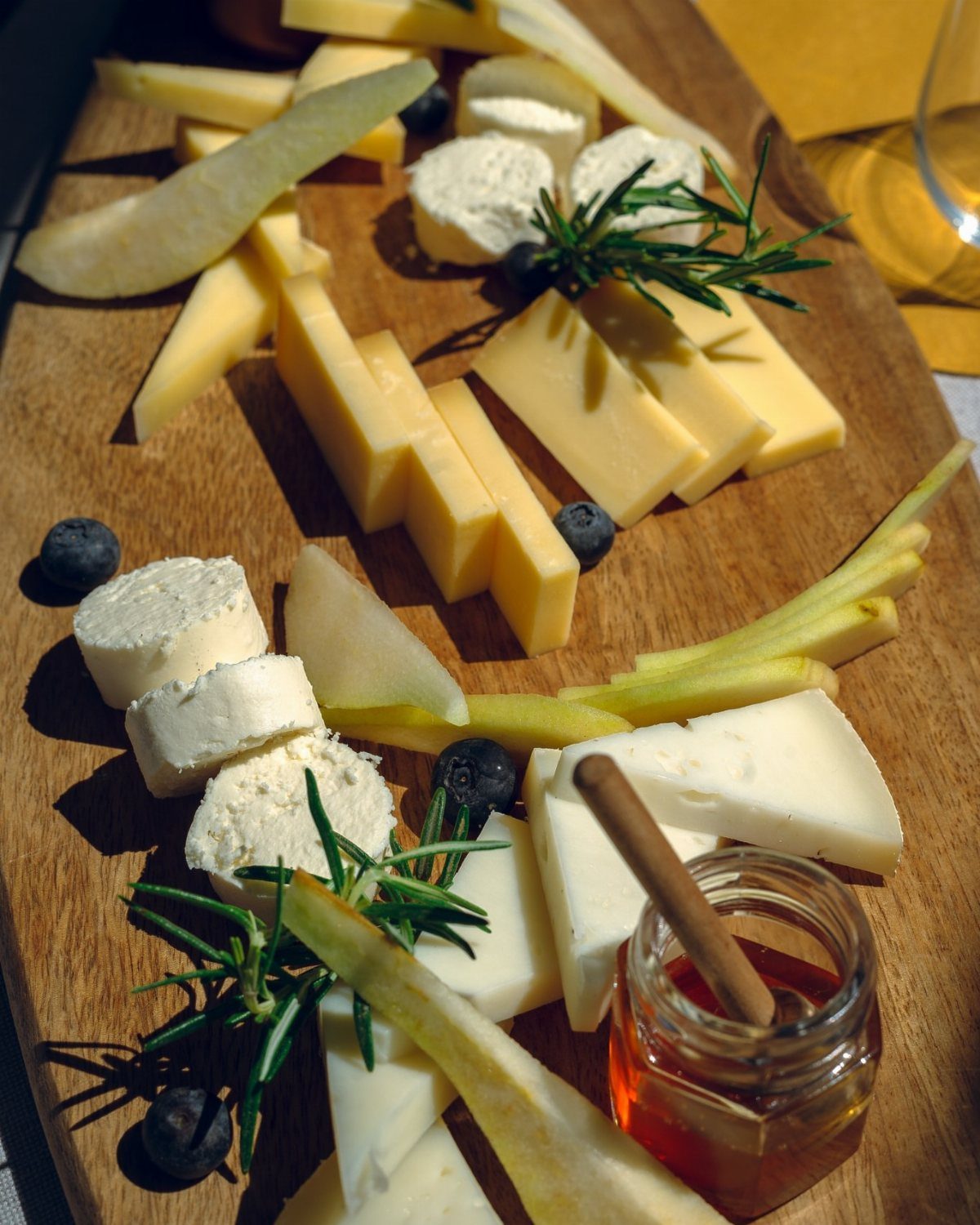 Cheese and fruit platter with pear, blueberries, and honey on a wooden board.