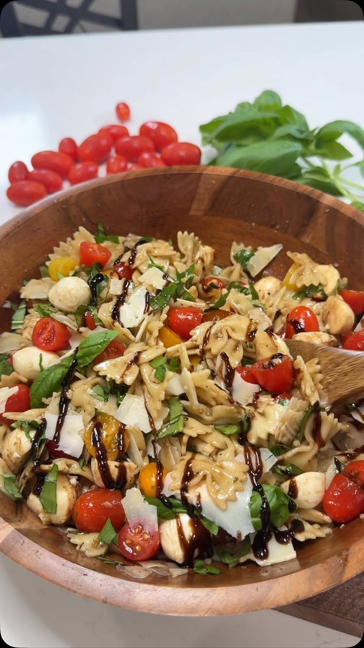 Farfalle pasta salad with cherry tomatoes, mozzarella, and balsamic glaze in wooden bowl