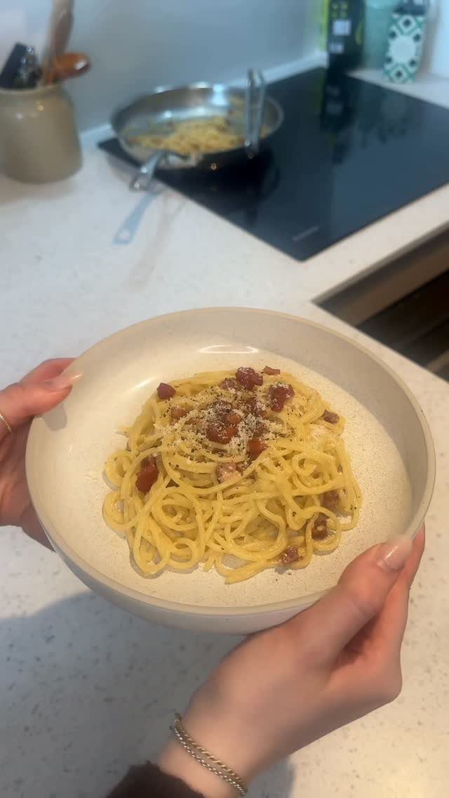 Spaghetti carbonara with pancetta and cheese held in a beige bowl in a kitchen.